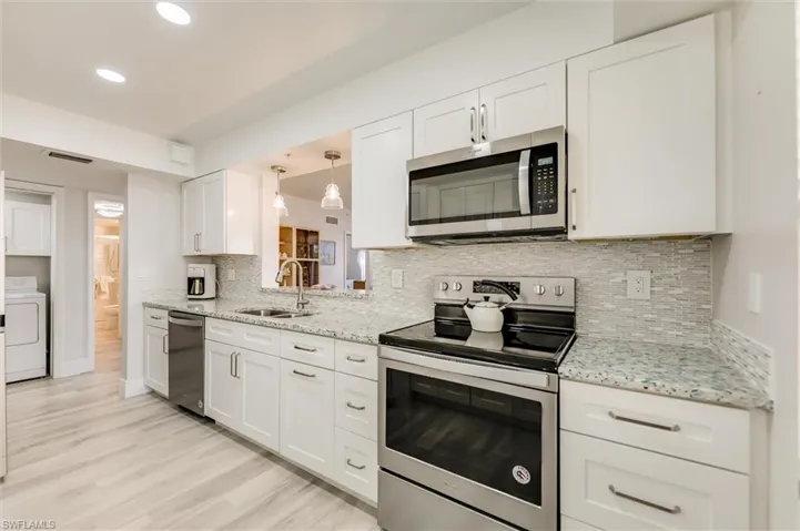 Kitchen featuring stainless steel appliances, white cabinetry, light stone counters, and recessed lighting