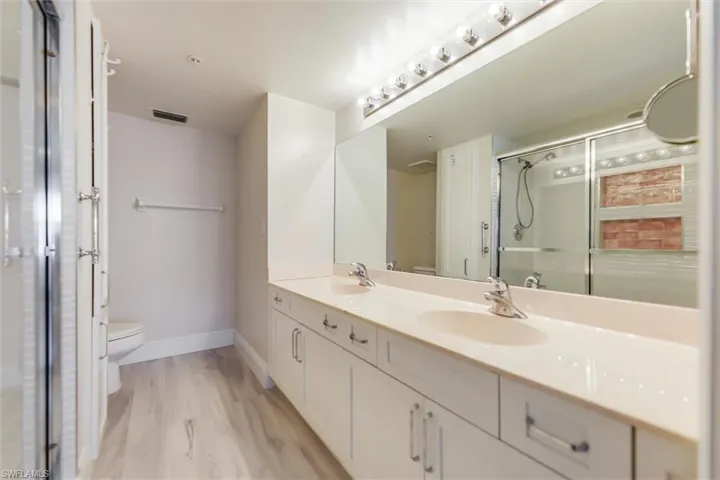 Full bathroom with double vanity, a stall shower, and light wood-style flooring