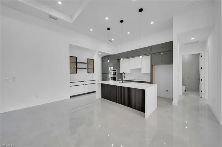 Kitchen with modern cabinets, recessed lighting, light countertops, a large island with sink, and decorative light fixtures
