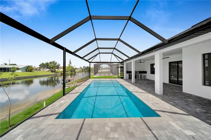 Outdoor pool with ceiling fan, a patio, a water view, and glass enclosure