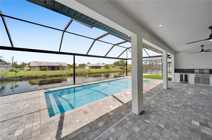 Swimming pool featuring an outdoor kitchen, a patio area, ceiling fan, a water view, and a lanai