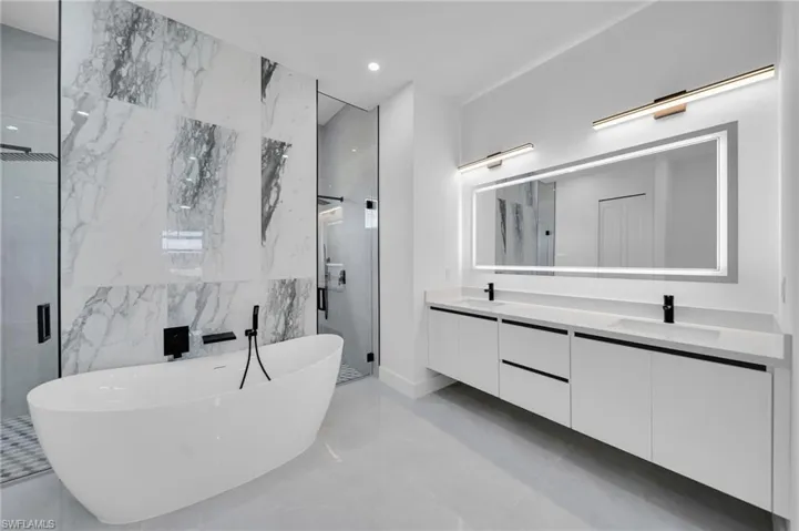 Full bathroom with a stall shower, marble tiled flooring, double vanity, and a freestanding bath