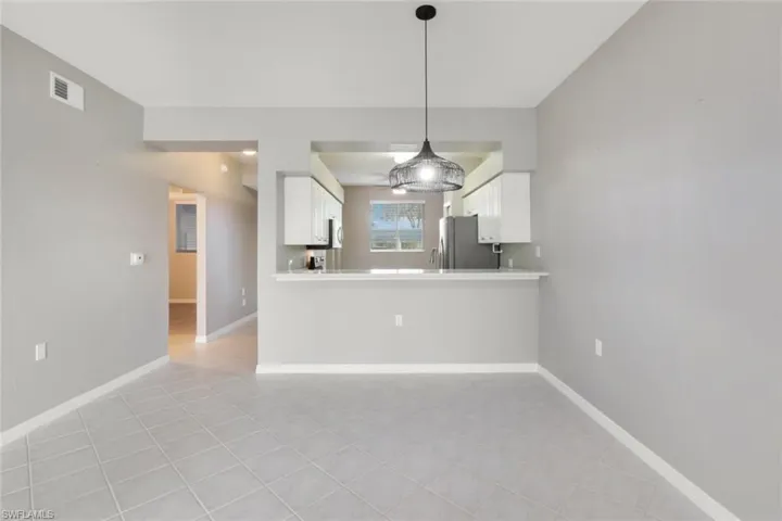 Kitchen featuring white cabinets, kitchen peninsula, stainless steel fridge, and light tile patterned floors