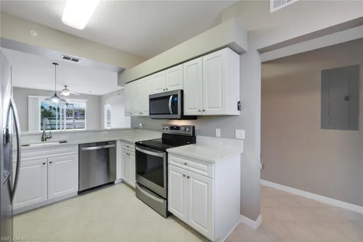 Kitchen featuring white cabinets, stainless steel appliances, sink, hanging light fixtures, and electric panel