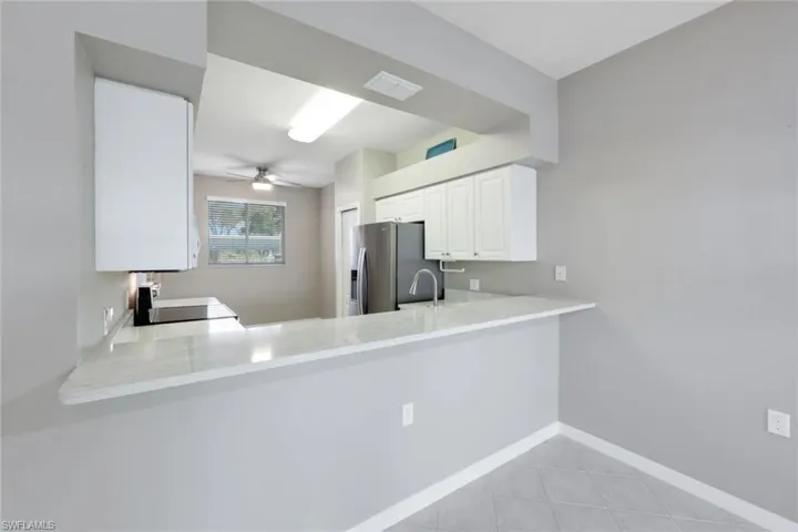 Kitchen with white cabinetry, sink, stainless steel fridge, kitchen peninsula, and ceiling fan