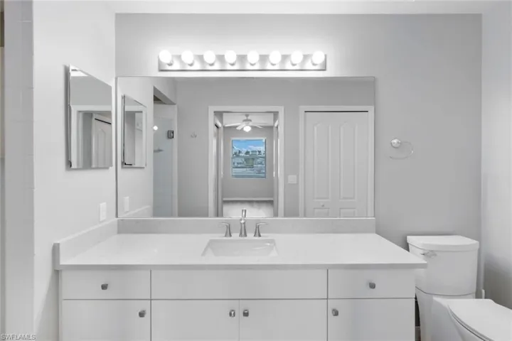 Bathroom with toilet, ceiling fan, an enclosed shower, and vanity