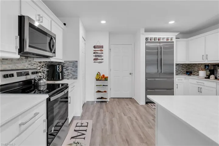 Kitchen featuring light hardwood / wood-style floors, stainless steel appliances, tasteful backsplash, and white cabinets