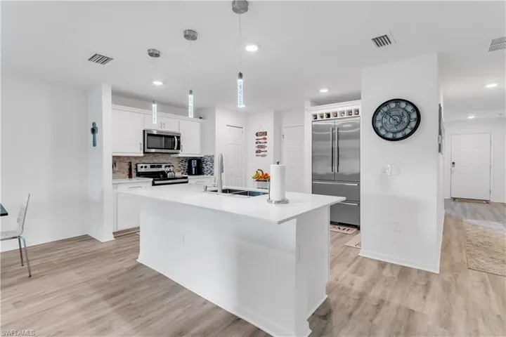 Kitchen with sink, appliances with stainless steel finishes, light hardwood / wood-style flooring, a kitchen island with sink, and tasteful backsplash