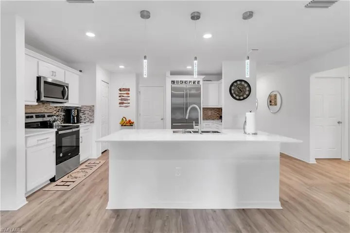Kitchen featuring tasteful backsplash, white cabinets, light hardwood / wood-style floors, sink, and stainless steel appliances
