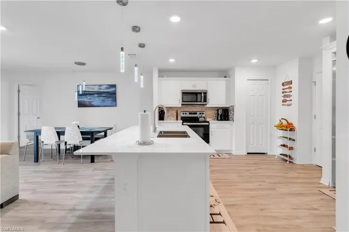 Kitchen featuring light hardwood / wood-style flooring, tasteful backsplash, white cabinets, appliances with stainless steel finishes, and decorative light fixtures