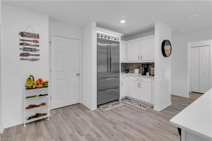 Kitchen featuring light wood-type flooring, stainless steel built in refrigerator, tasteful backsplash, and white cabinetry
