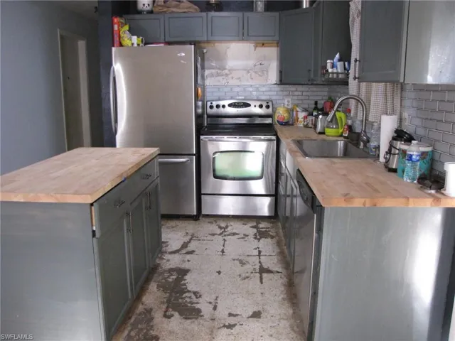 Kitchen with wooden counters, a center island, stainless steel appliances, decorative backsplash, and sink