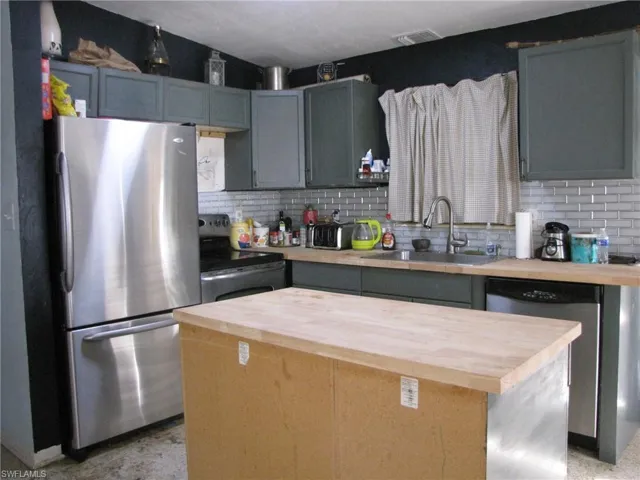 Kitchen with butcher block counters, backsplash, a center island, stainless steel appliances, and sink