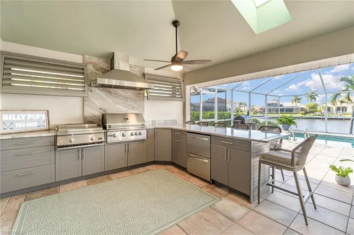 Summer kitchen featuring wall chimney exhaust hood, kitchen peninsula, stainless steel fridge, a kitchen bar, and a water view