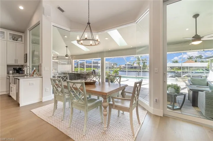 Dining area featuring a water view, lofted ceiling with skylight, light wood-type flooring, and ceiling fan with notable chandelier