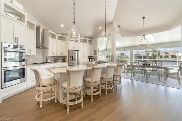 Kitchen featuring wall chimney range hood, hanging light fixtures, appliances with stainless steel finishes, gas cooktop a kitchen island with sink, and light wood-type flooring