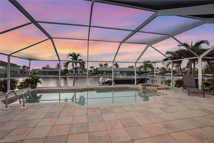 Pool at dusk featuring a patio, an in ground hot tub, a water view, and screen enclosure