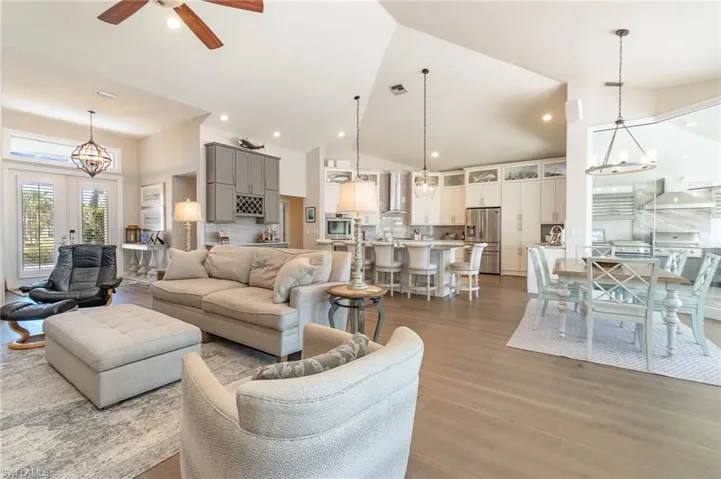 Living room featuring french doors, high vaulted ceiling, ceiling fan with notable chandelier, and light wood-type flooring