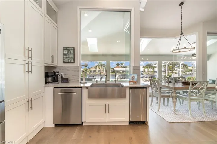 Kitchen with dishwasher, white cabinets, pendant lighting, and light hardwood / wood-style floors