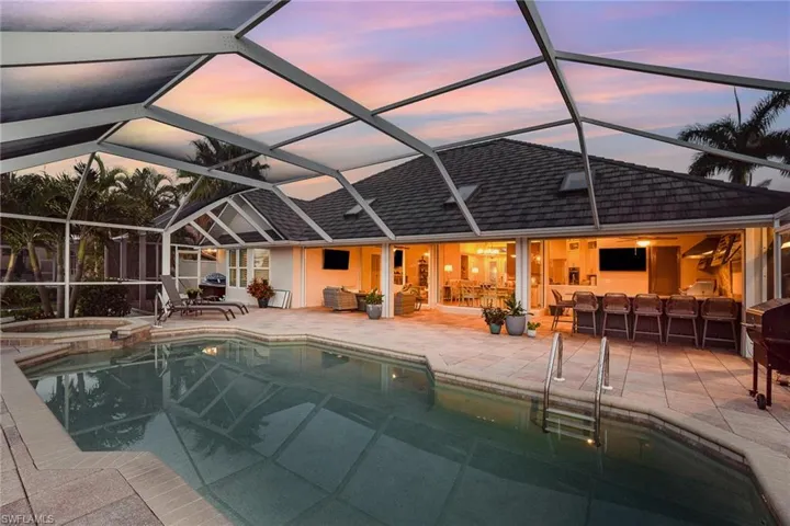 Pool at dusk with an in ground hot tub, a patio area, screen enclosure, and an outdoor area