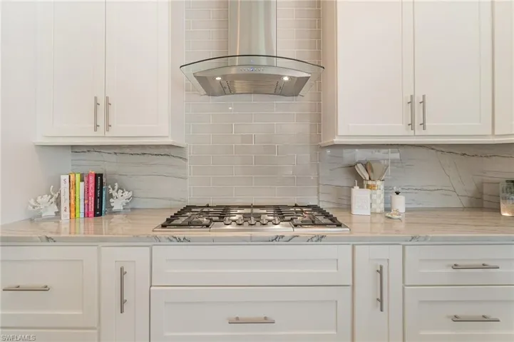 Kitchen featuring light stone counters, gas cooktop range hood, decorative backsplash, and white cabinets