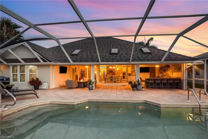 Back house at dusk featuring a patio, an outdoor bar, and a lanai