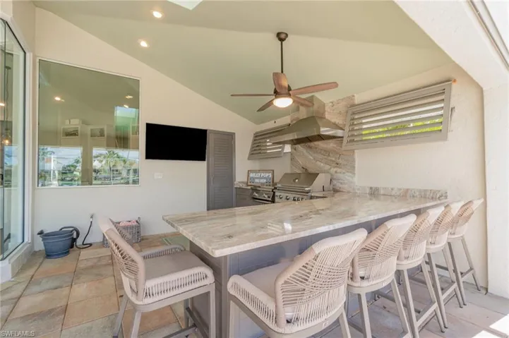 Summer kitchen with lofted ceiling, a breakfast bar, light stone countertops, and kitchen peninsula