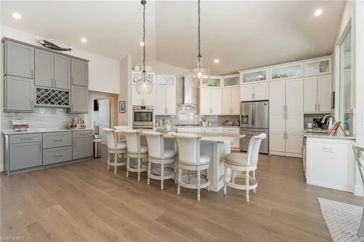 Kitchen with wall chimney exhaust hood, vaulted ceiling, gray cabinetry, and stainless steel appliances