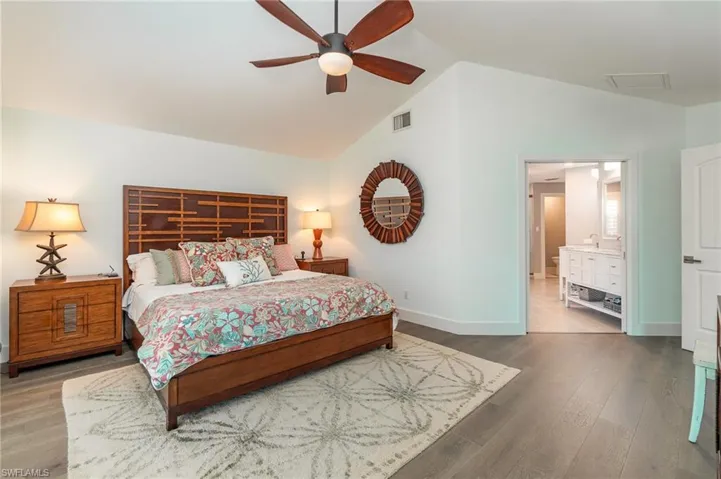 Bedroom featuring hardwood / wood-style floors, vaulted ceiling, ensuite bathroom, and ceiling fan