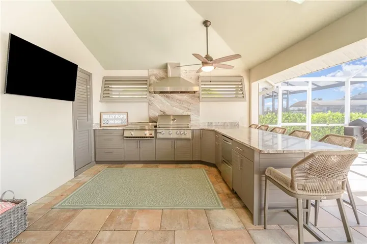 Summer kitchen featuring gray cabinetry, wall chimney exhaust hood, vaulted ceiling, and kitchen peninsula