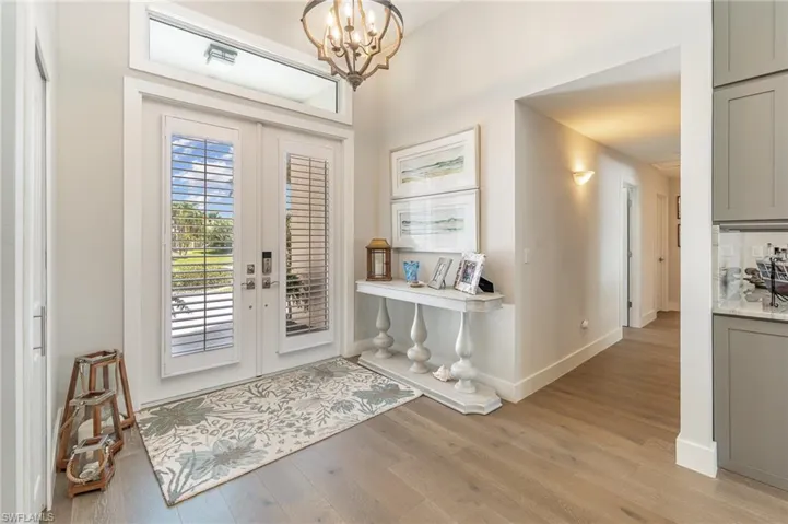 Foyer entrance with an inviting chandelier, french doors, and light wood-type flooring