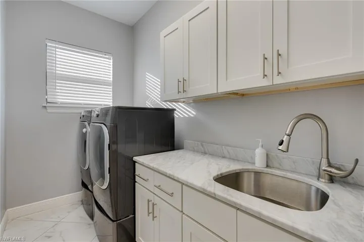 Laundry area featuring independent washer and dryer, cabinet space, and light marble finish flooring