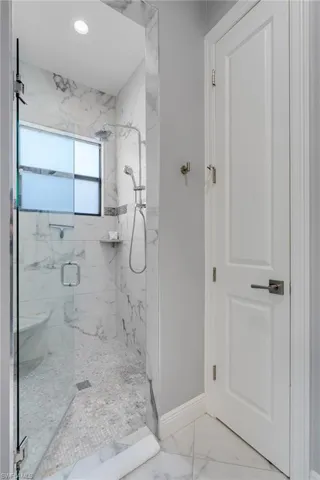 Bathroom featuring a marble finish shower, marble look tiles, and recessed lighting