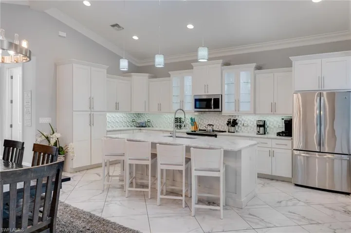 Kitchen with stainless steel appliances, a kitchen bar, light marble finish floors, lofted ceiling, and light stone counters