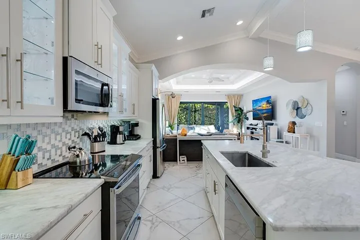 Kitchen featuring white cabinets, stainless steel appliances, a kitchen island with sink, glass fronted cabinets, and crown molding