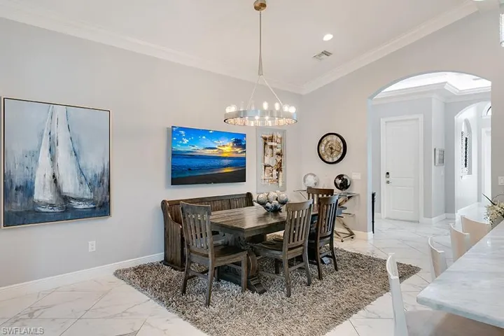 Dining area featuring arched walkways, light marble finish floors, crown molding, and hanging lights