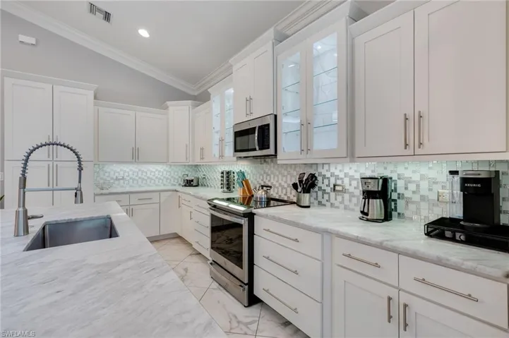 Kitchen with vaulted ceiling, stainless steel appliances, tasteful backsplash, white cabinetry, and light stone counters