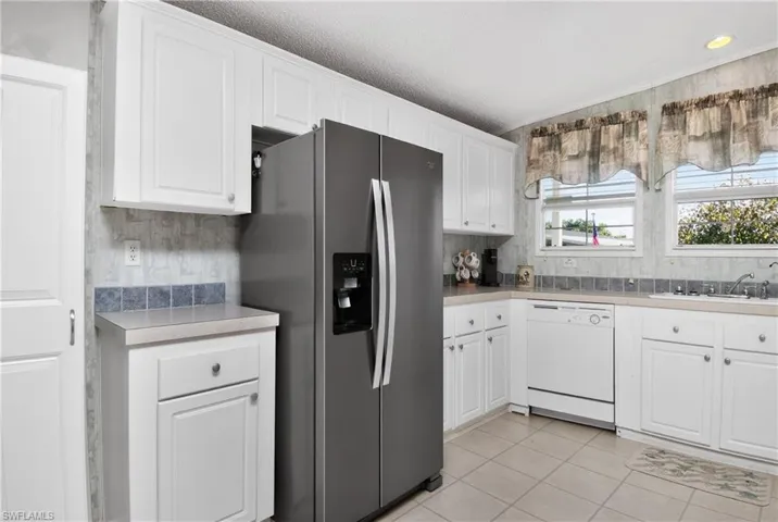 Kitchen with stainless steel fridge with ice dispenser, white cabinetry, dishwasher, light countertops, and light tile patterned floors