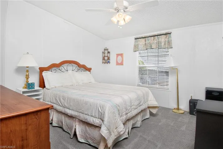 Bedroom with dark colored carpet, a textured ceiling, and ceiling fan