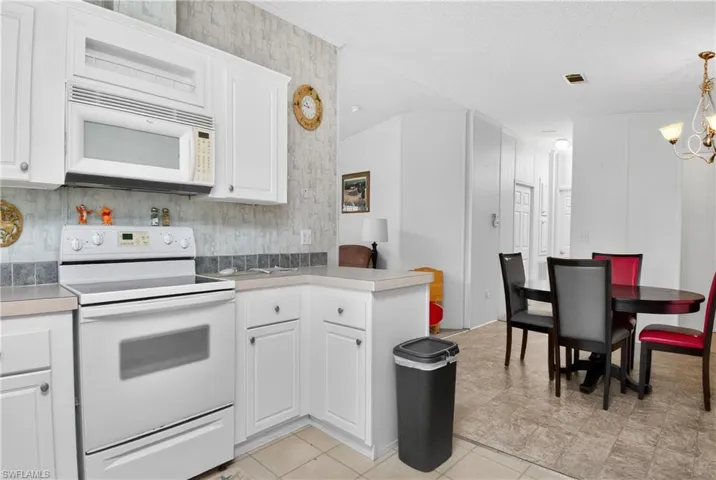 Kitchen with white appliances, light countertops, white cabinetry, a peninsula, and crown molding