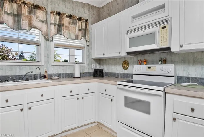Kitchen with white appliances, white cabinetry, light countertops, wallpapered walls, and light tile patterned floors