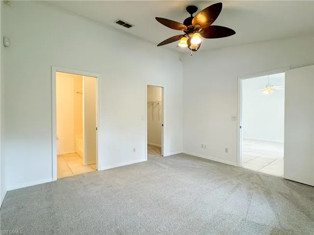 Unfurnished bedroom featuring a spacious closet, light carpet, ceiling fan, and connected bathroom