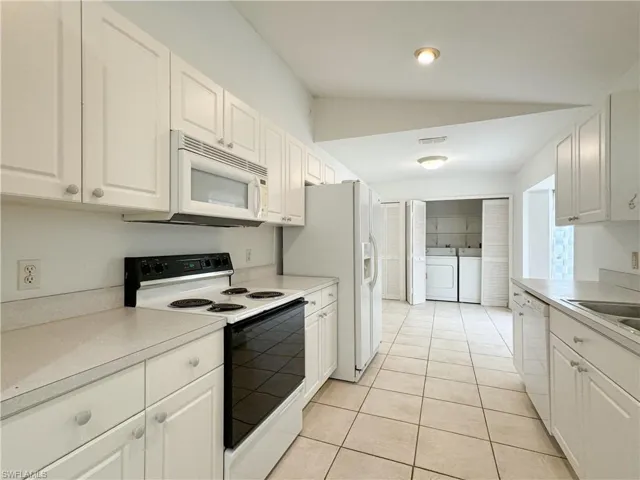 Kitchen with light tile patterned flooring, lofted ceiling, white appliances, white cabinets, and washing machine and clothes dryer