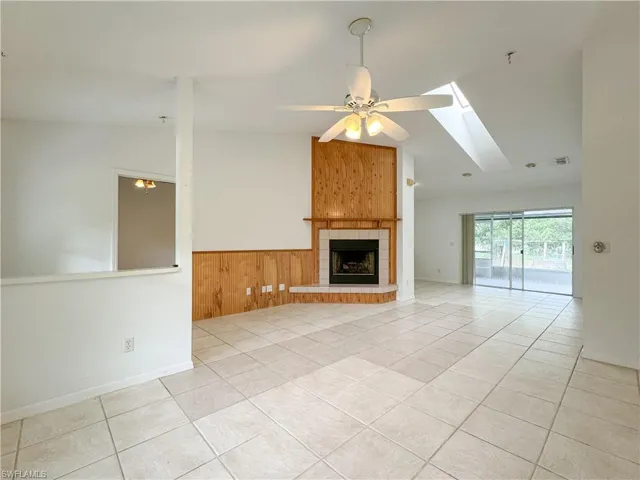 Unfurnished living room with light tile patterned floors, lofted ceiling with skylight, ceiling fan, and a tiled fireplace