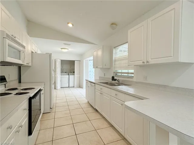 Kitchen featuring white cabinetry, lofted ceiling, white appliances, light tile patterned floors, and sink