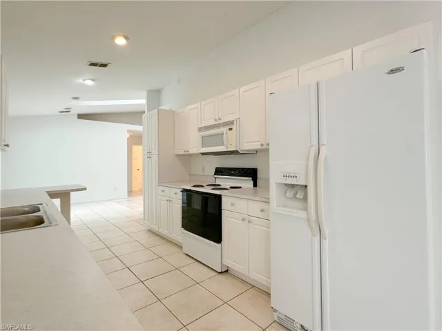 Kitchen with sink, white cabinetry, light tile patterned floors, and white appliances