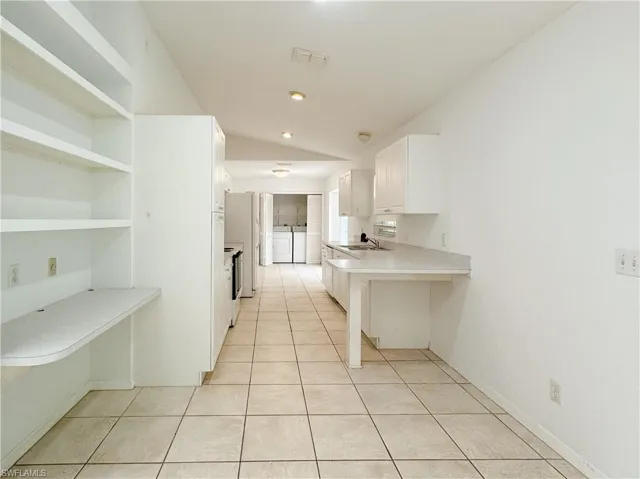 Kitchen with sink, white cabinetry, light tile patterned floors, and washing machine and clothes dryer