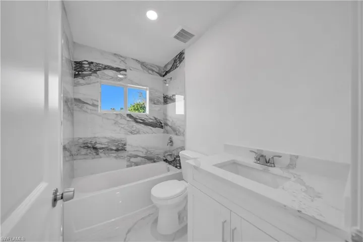 Bathroom with vanity, bathing tub / shower combination, marble finish flooring, and recessed lighting