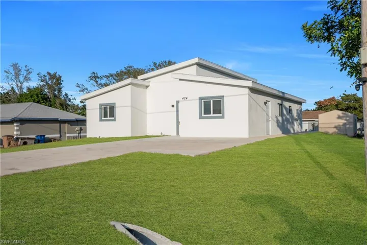 Rear view of house with a yard, concrete driveway, and stucco siding