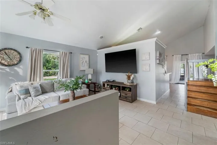Living room with ceiling fan, light tile patterned flooring, and lofted ceiling